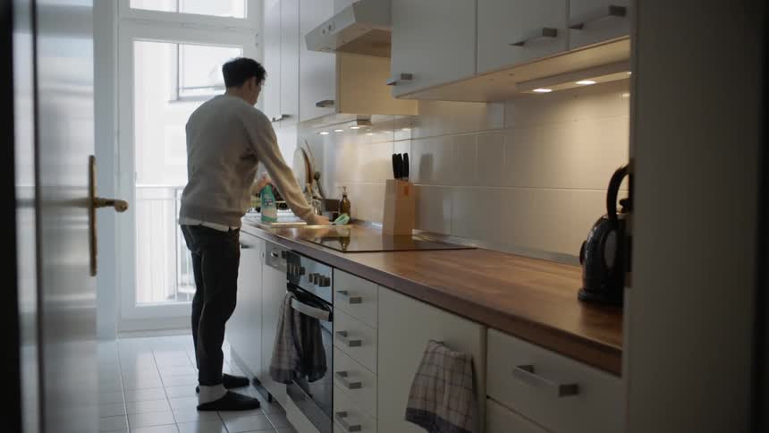 Man wearing sweatshirt and slippers cleans kitchen counter
