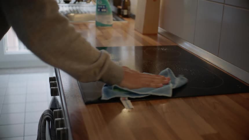 A person wiping down a stove top with a washcloth