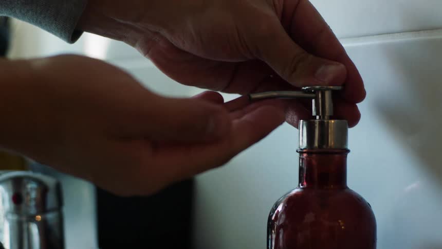 Person dispenses soap from bottle near sink faucet