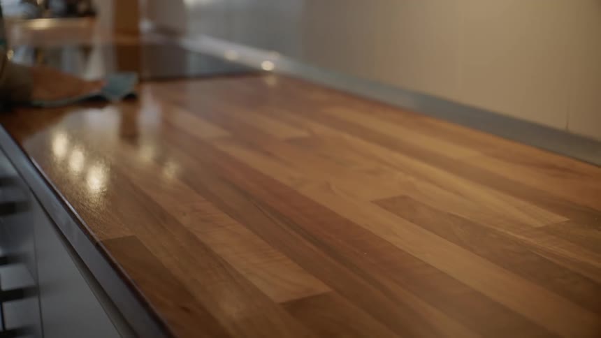 Males wipes the butcher block counter top in the kitchen with a blue cloth