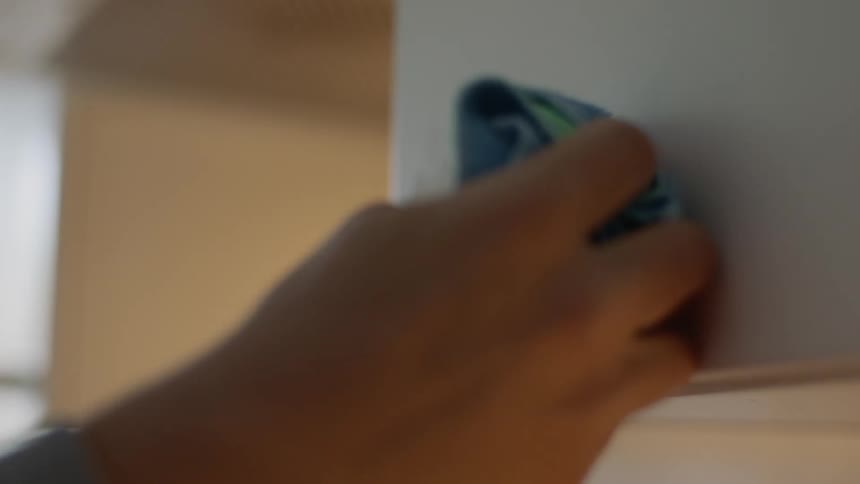 A persons hand with a rag wiping down a cupboard handle