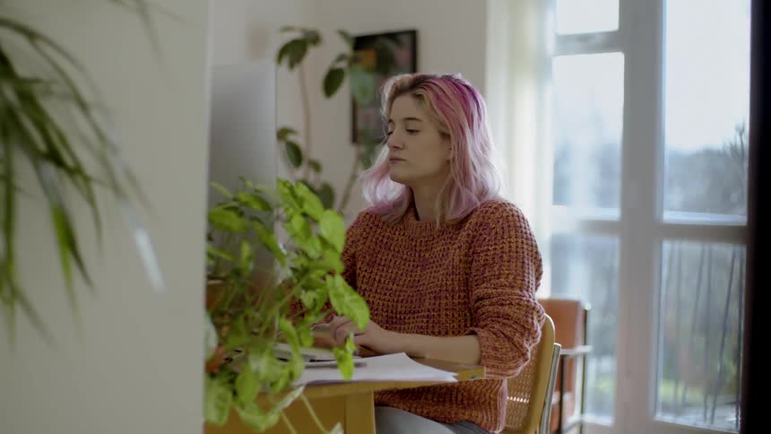 A pink haired female at her computer in her living room