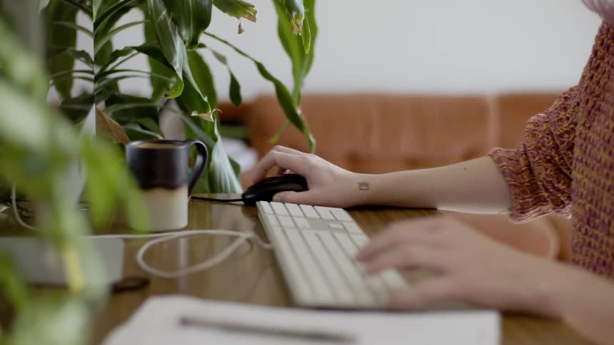 A woman types on a keyboard and uses a computer mouse at a desk