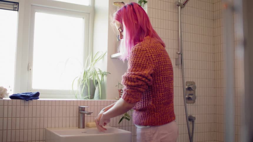 Pink haired woman washes her hands with soap in the bathroom