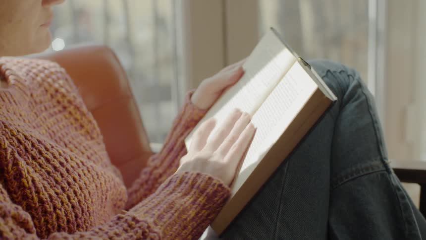Woman sits with her knees up as she reads a book