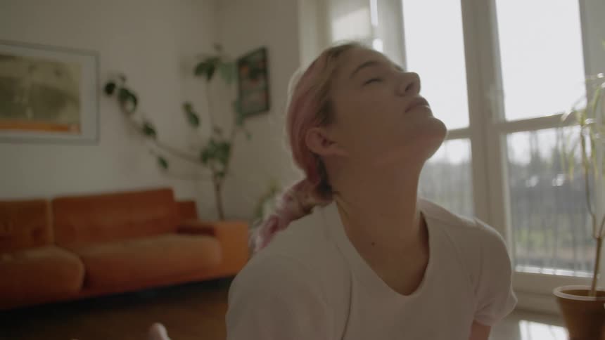 A pink haired woman performing stretches in her living room