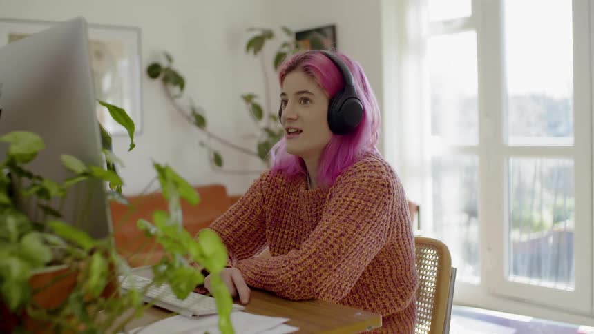 A pink haired female at her computer in her living room