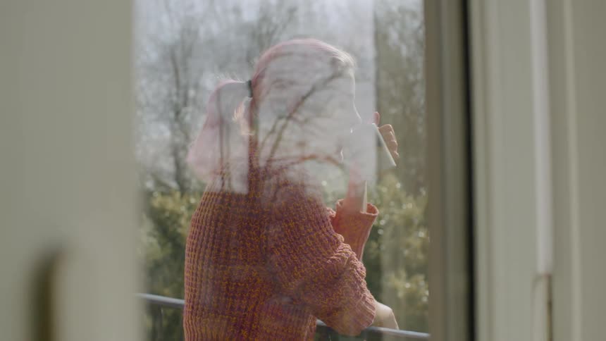 A woman stands outside on a balcony drinking from a mug