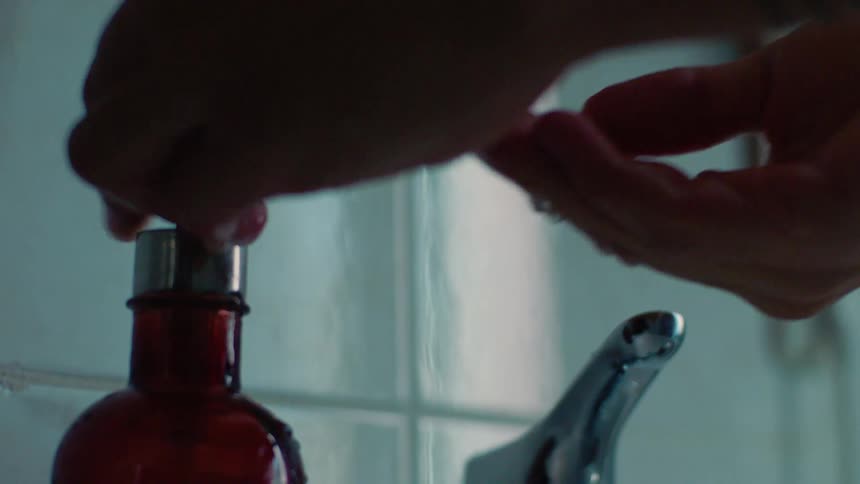A man pumps soap from a dispenser into his hands and rubs them together while allowing water to run from the faucet into a sink