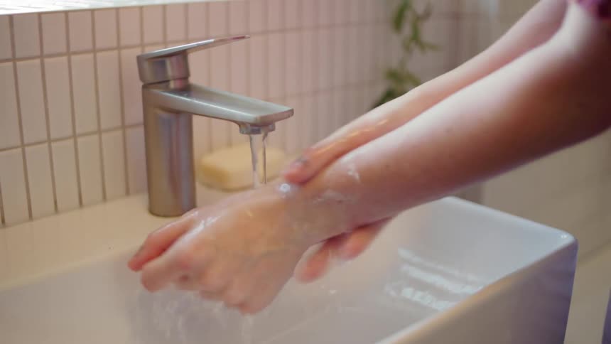 Woman washing hands under running water in sink