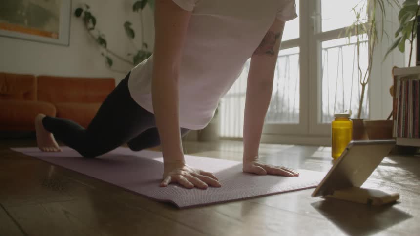 A pink haired woman performing stretches in her living room