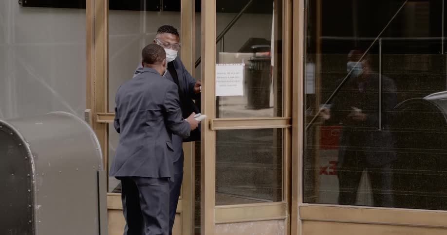 Two men talk outside a building as another person walks out