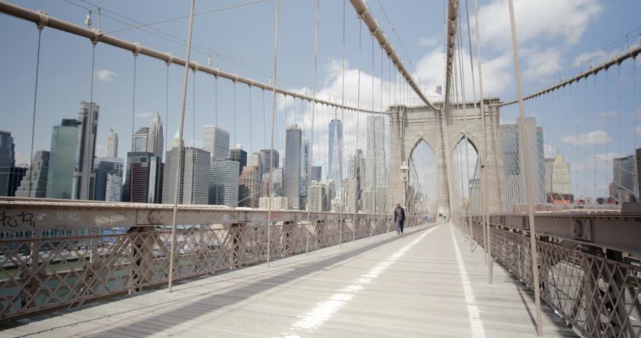 Pedestrian crosses bridge away from city downtown as cars pass along highway nearby