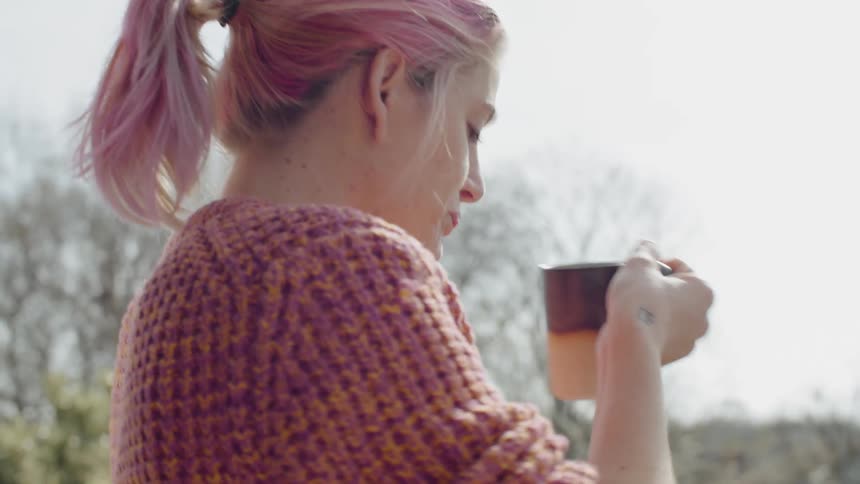Woman with pink hair drinking coffee outside on balcony