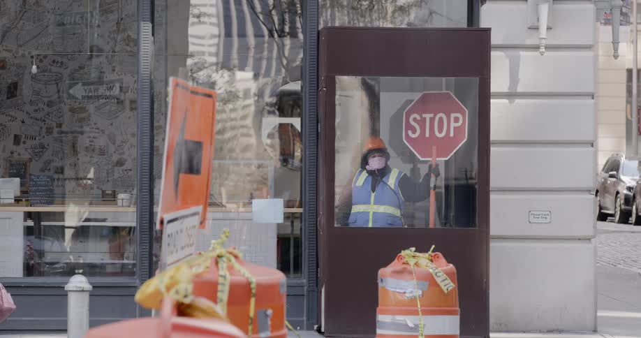 Person wearing a vest holds a stop sign while standing inside a booth