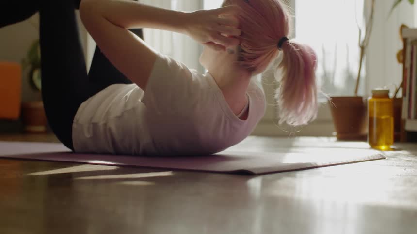Female wearing exercise apparel lays on a yoga mat while performing bicycle sit ups