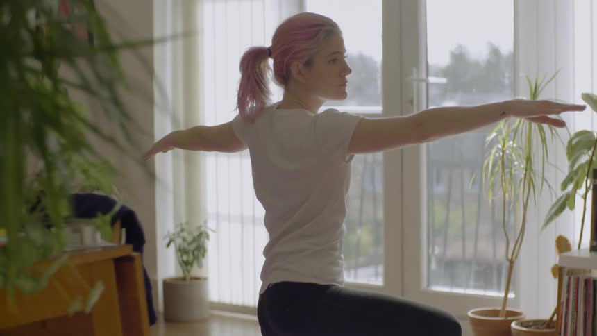 Woman with pink hair practices yoga on a yoga mat