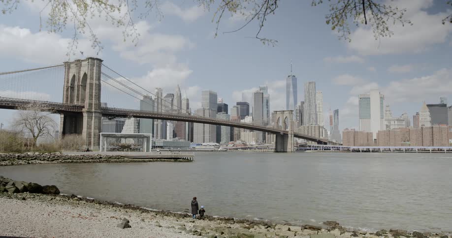 A woman and her child stand along a river bank that runs by downtown