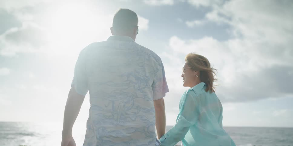 Man and woman holding hands stand on the coast and watch the waves on a sunny day