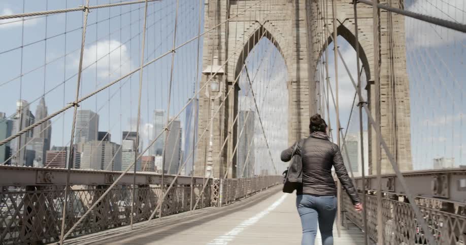 Woman walks across brooklyn bridge towards manhattan