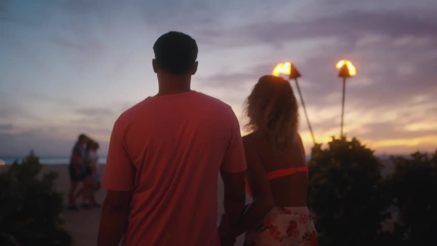 Couple vacationing in hawaii goes to a beach party at sunset