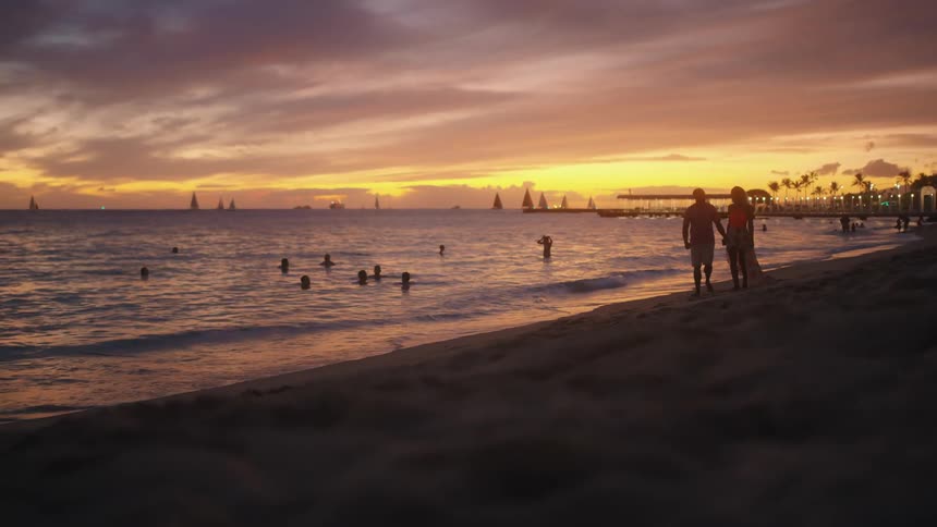 Couple walking holding hands on beach at sunset