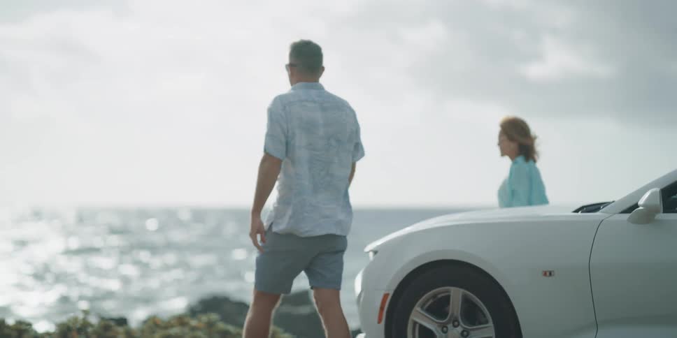 Older couple exits car and walks toward ocean holding hands
