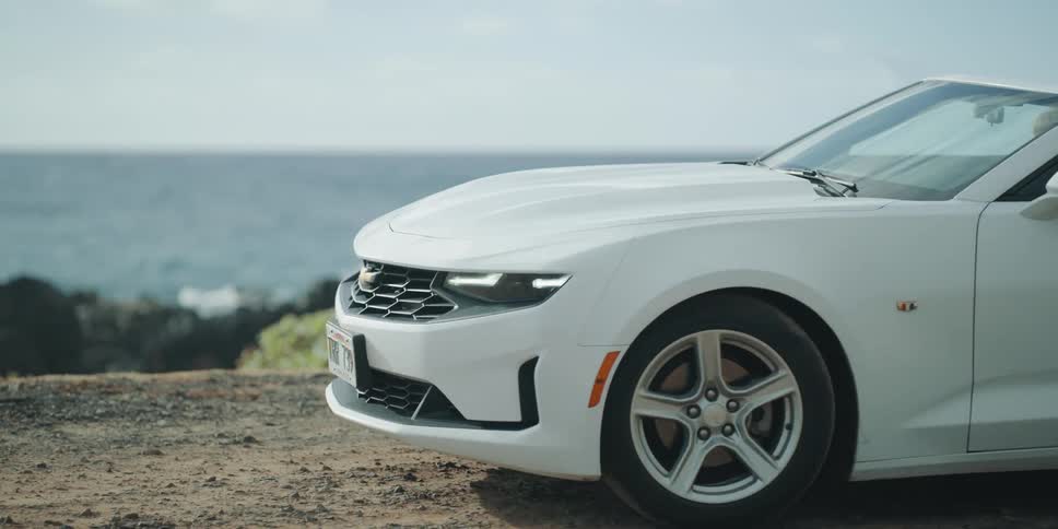 White convertible driving up and parking cliff side overlooking the coast