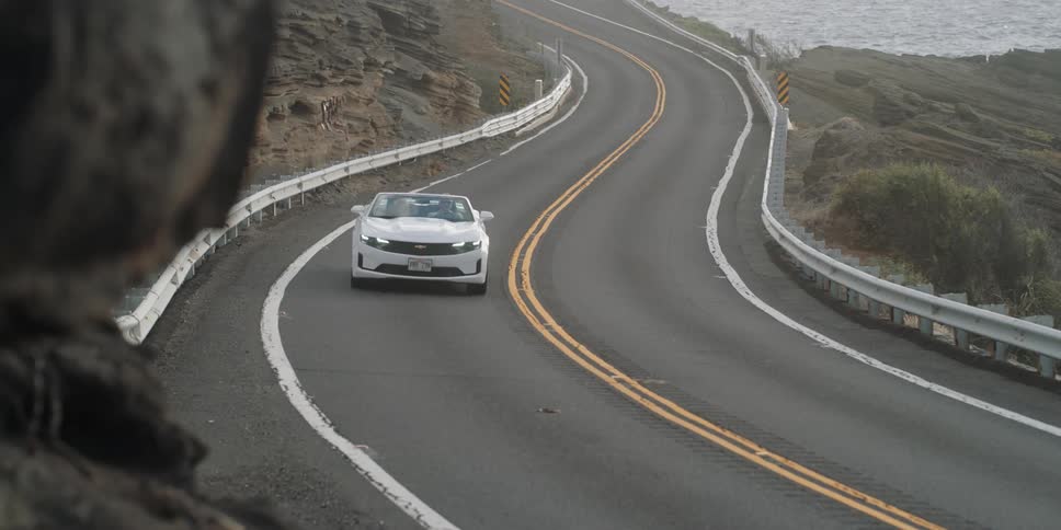 Cars drive along winding road near water
