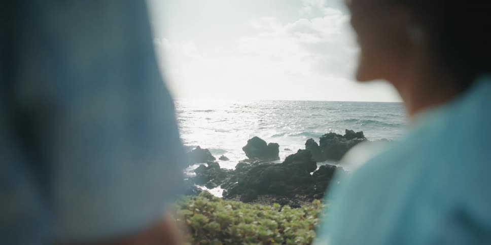 A man and woman stand on the shore and look out at the water