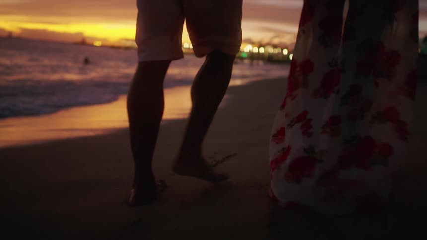 Black man and white woman walk along the sand beach at sunset next to the sea