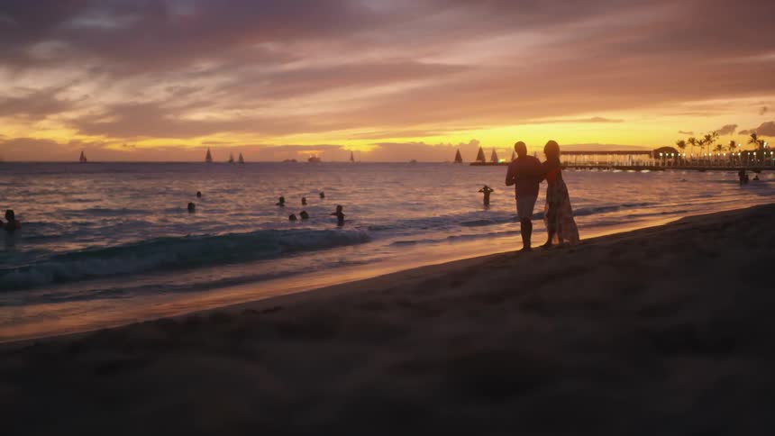 Couple walks on beach at sunset