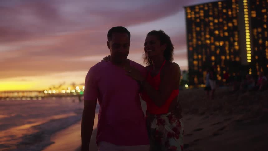 Romantic couple strolling by the shoreline at sunset at a resort