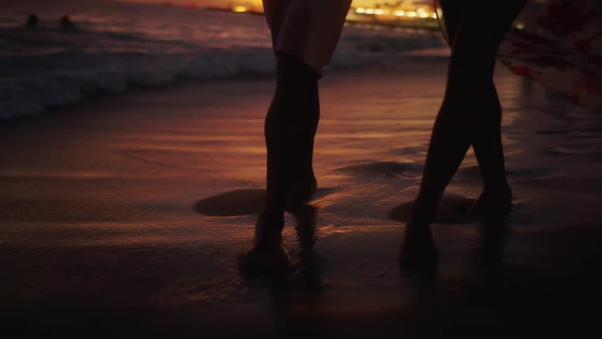 A couple embracing while walking along a beach at sunset