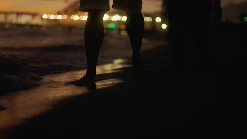 Couple walks through water on beach at night