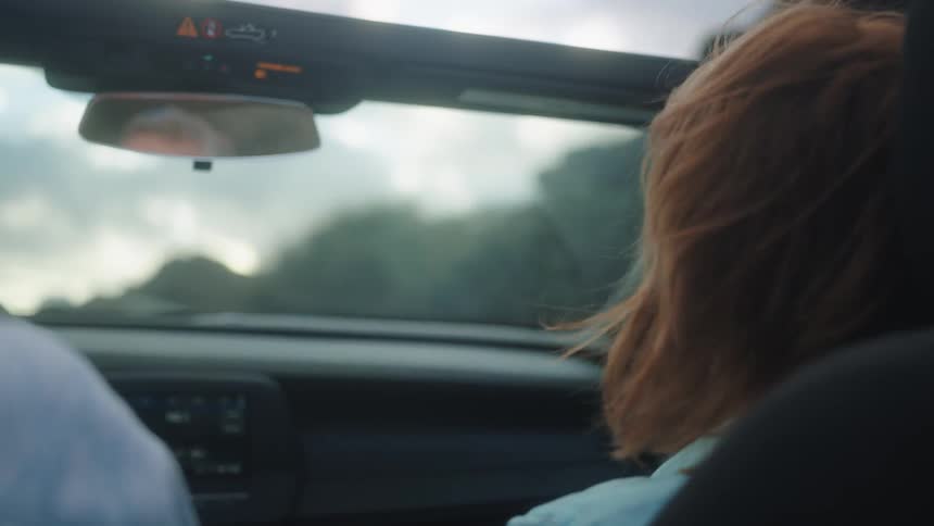 A man and woman traveling in a car with its roof down during the day