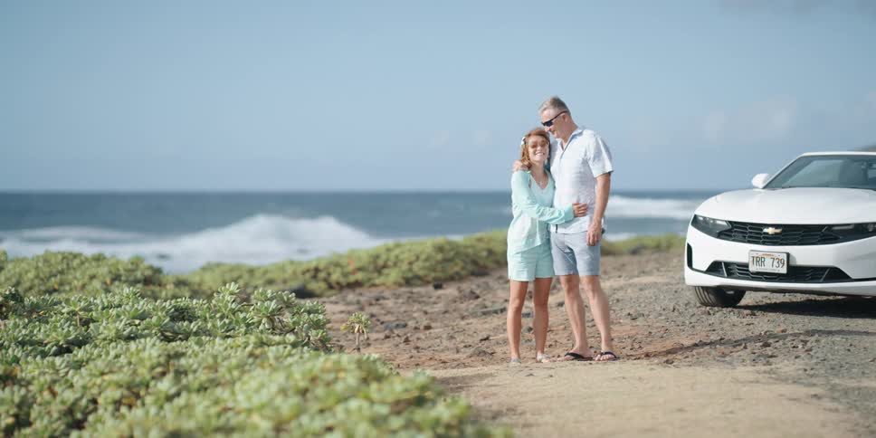 A husband and wife park on the beach and embrace along the shore