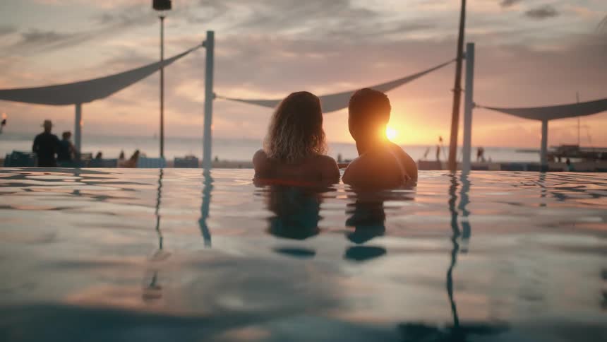 A man and woman relax in an ocean side pool together admiring the sunset