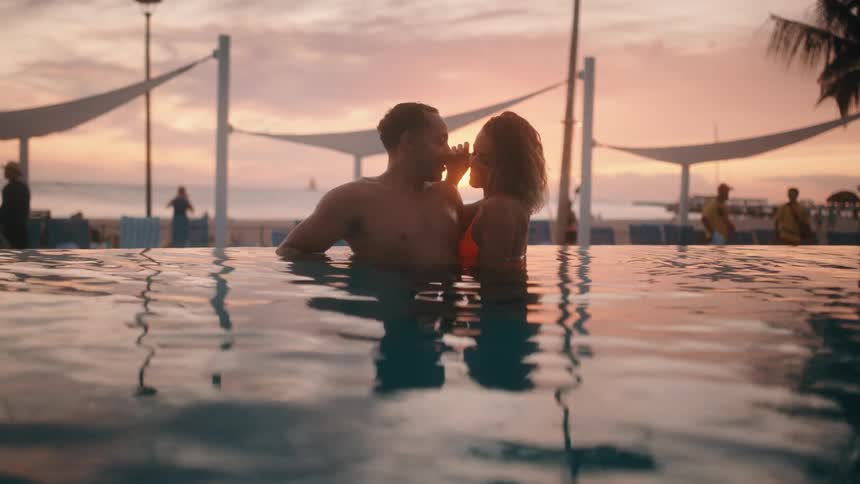 White woman and black man swim in the pool at dusk