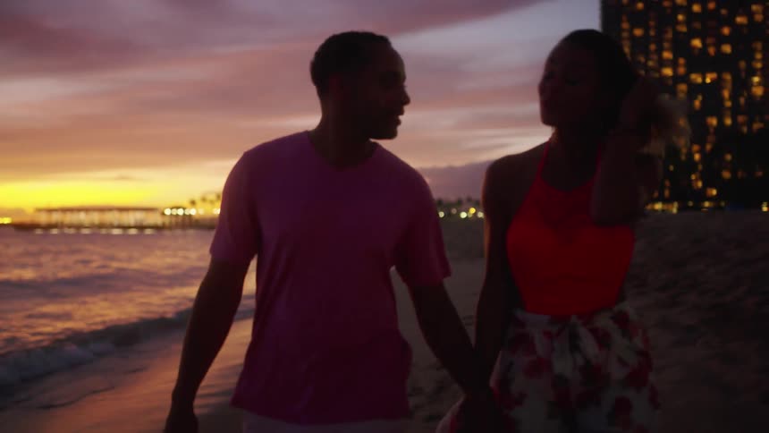 Couple hold hands while walking on the sands of a beach at sunset