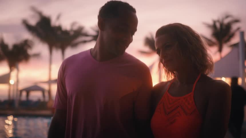 Black man and white woman stroll along on the promenade at sunset