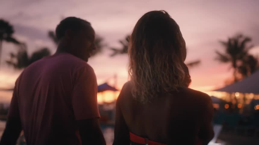 A man and a woman walking holding hands by a swimming pool
