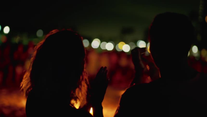 A crowd of people watch a performer toss a flaming baton