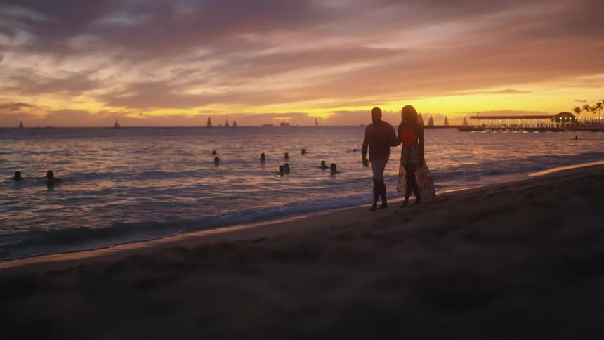 Husband and wife walk on the yellow sand beach at sunset next to the sea