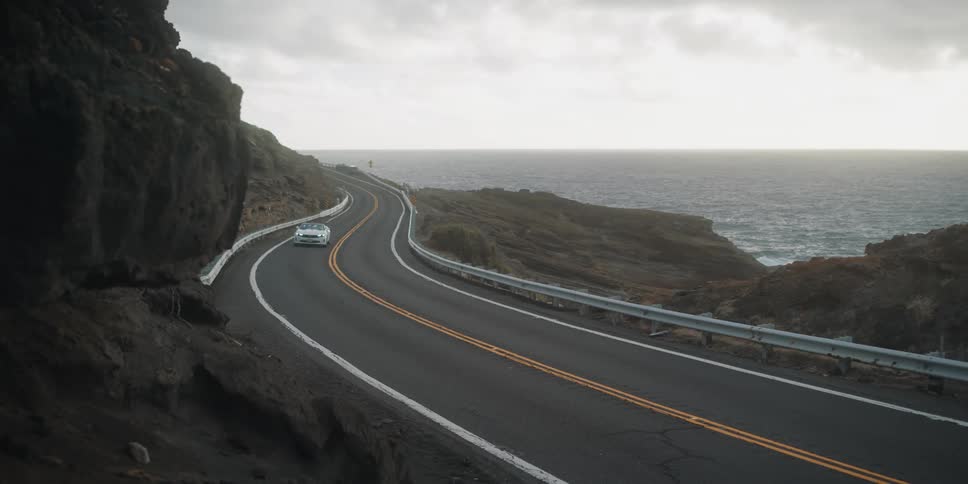 White convertible driving on road alongside the coast