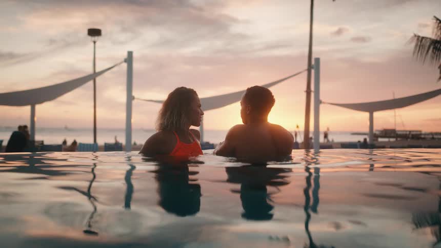 Couple relaxing in a pool at sunset at a beach resort