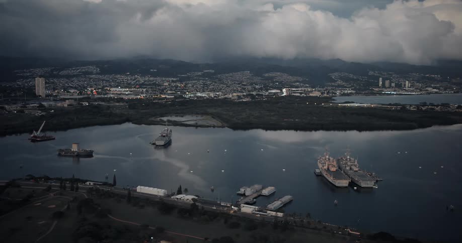 Cars travel on a coastal road past a harbor with ships anchored