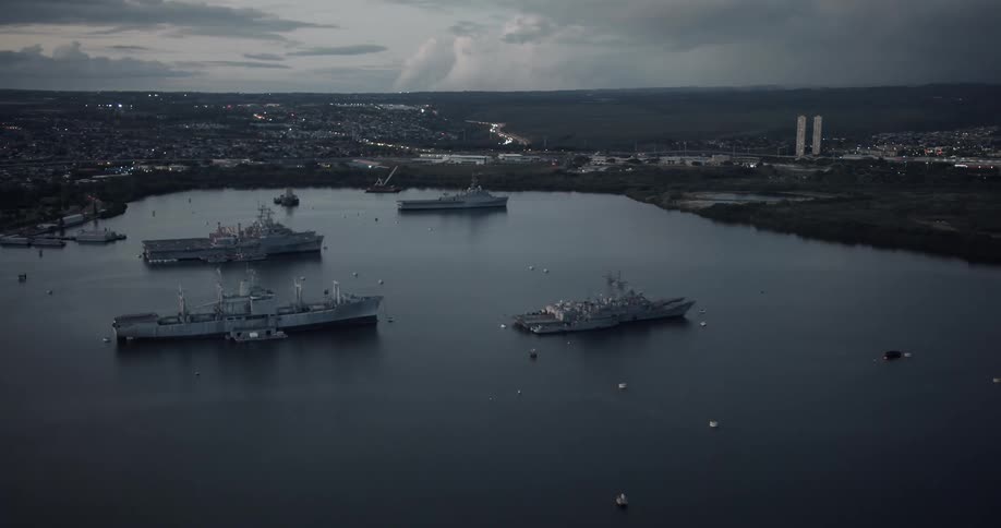 Naval vessels occupy bay near city under a cloudy sky