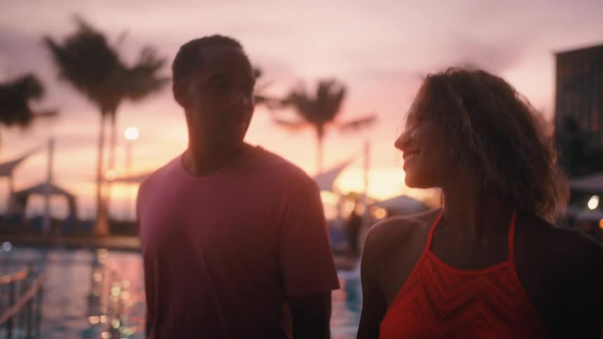 A man and woman walk along holding hands at a resort