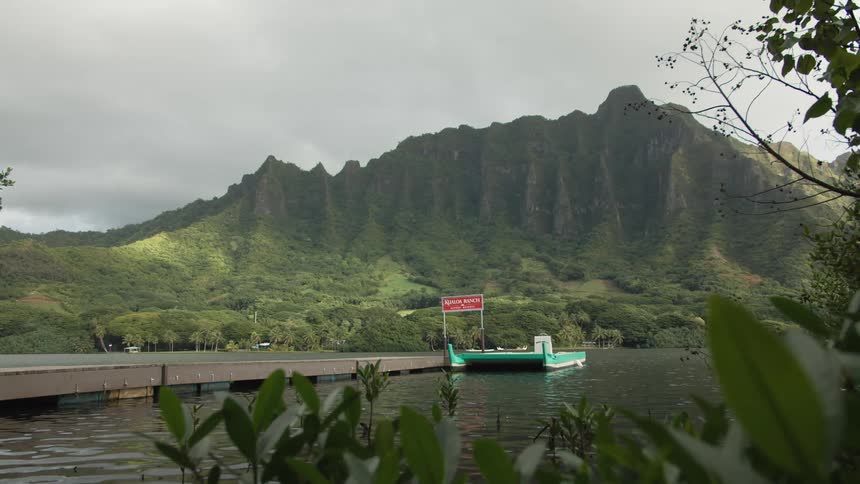 Small boat at end of dock in hawaii in front of mountains